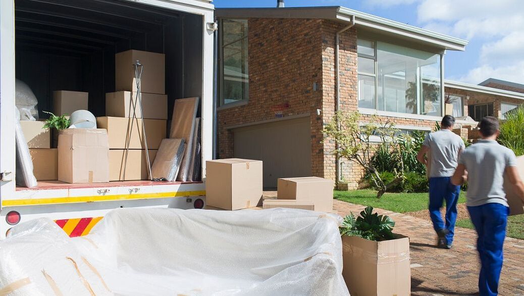 Two movers unloading a moving van into a residential home.